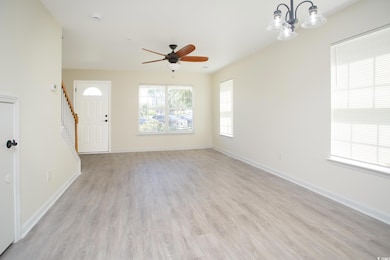 Unfurnished living room featuring light wood-style flooring, stairs, ceiling fan, and a chandelier