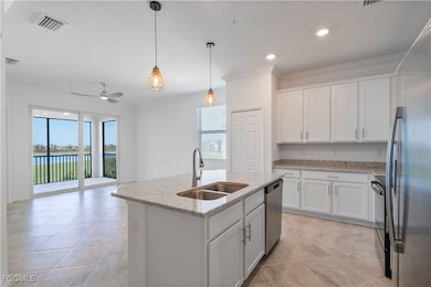 Kitchen with white cabinets, ornamental molding, appliances with stainless steel finishes, hanging light fixtures, and light stone countertops