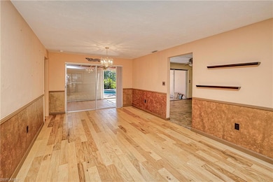 Spare room featuring a wainscoted wall, light wood finished floors, a chandelier, and a ceiling fan
