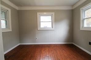 Empty room with dark wood-style floors, crown mold