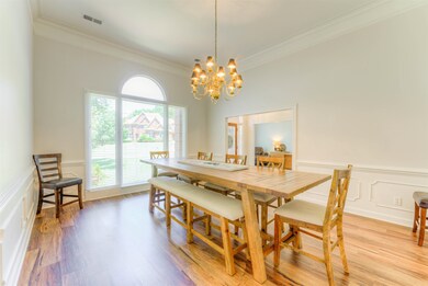 Dining space with ornamental molding, a decorative wall, a chandelier, a wainscoted wall, and light wood finished floors