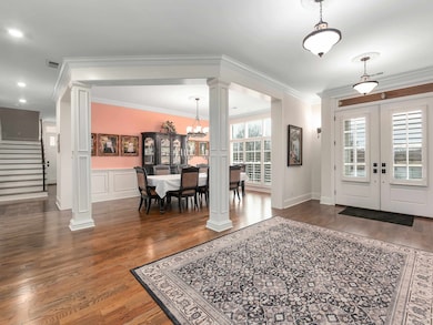 Foyer with decorative columns, crown molding, wood finished floors, stairs, and a chandelier