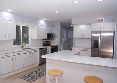 Kitchen with appliances with stainless steel finishes, a kitchen bar, decorative backsplash, light wood-style flooring, and white cabinetry