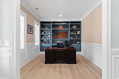 Home office featuring light wood finished floors, wainscoting, crown molding, and built in shelves