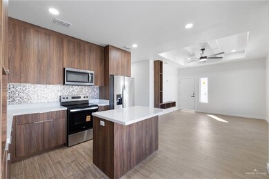 Kitchen featuring modern cabinets, a tray ceiling, appliances with stainless steel finishes, a kitchen island, and decorative backsplash