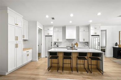 Kitchen featuring custom range hood, high quality fridge, light wood finished floors, white cabinets, and recessed lighting