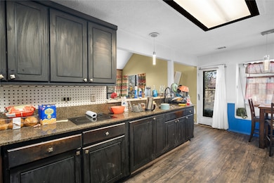 Kitchen with dark stone countertops, decorative backsplash, dark wood-type flooring, a textured ceiling, and pendant lighting