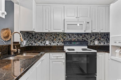 Kitchen with white appliances, white cabinets, and dark stone countertops