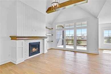 Unfurnished living room with high vaulted ceiling, light wood finished floors, visible vents, a brick fireplace, and a notable chandelier