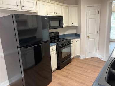 Kitchen featuring black appliances, light wood-style flooring, white cabinets, and dark countertops