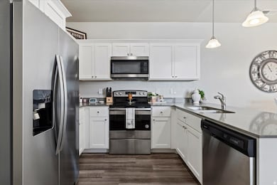 Kitchen with stainless steel appliances and finishes, white cabinets, pendant lighting, and a peninsula