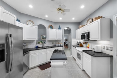 Kitchen featuring stainless steel appliances, arched walkways, recessed lighting, backsplash, and dark countertops