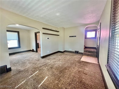 Empty room with dark colored carpet, arched walkways, a textured ceiling, and stairway
