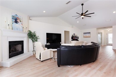 Living area featuring a ceiling fan, light wood finished floors, vaulted ceiling, a fireplace with raised hearth, and recessed lighting