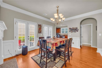 Dining area with arched walkways, ornamental molding, french doors, light wood finished floors, and a chandelier