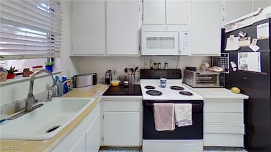 Kitchen with range with electric stovetop, white cabinetry, white microwave, and light countertops