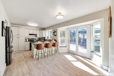 Kitchen with a kitchen bar, stainless steel appliances, a peninsula, white cabinetry, and light wood-style flooring