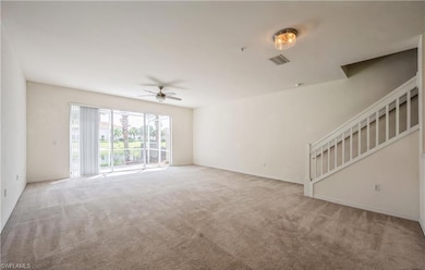 Unfurnished living room featuring carpet floors, ceiling fan, and stairway