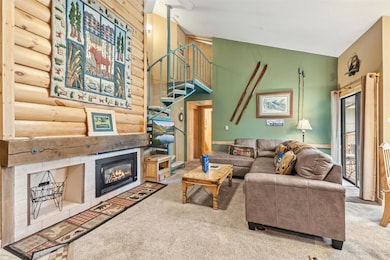 Living room with carpet floors, a glass covered fireplace, and stairs