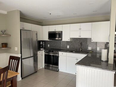 Kitchen featuring appliances with stainless steel finishes, dark stone counters, light tile patterned flooring, white cabinetry, and decorative backsplash