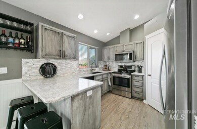 Kitchen with stainless steel appliances, a peninsula, light wood-style flooring, backsplash, and lofted ceiling