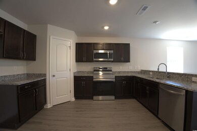 Kitchen featuring appliances with stainless steel finishes, light stone counters, wood finished floors, dark brown cabinets, and recessed lighting