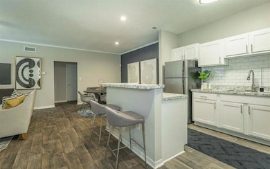 Kitchen with dark wood-style flooring, decorative backsplash, a textured ceiling, white cabinetry, and a kitchen breakfast bar