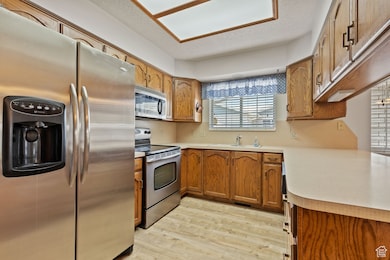 Kitchen with appliances with stainless steel finishes, brown cabinetry, light wood-style floors, and light countertops