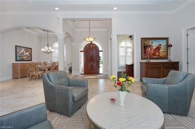 Living room with ceiling fan with notable chandelier, ornate columns, and crown molding