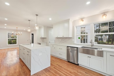 Kitchen with hanging light fixtures, decorative backsplash, white cabinetry, an island with sink, and dishwasher