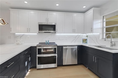 Kitchen featuring white cabinetry, a sink, light stone counters, and appliances with stainless steel finishes