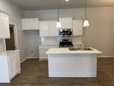 Kitchen with stainless steel appliances, white cabinets, hanging light fixtures, tasteful backsplash, and a kitchen island with sink