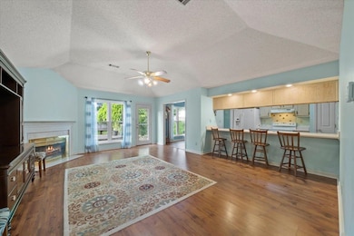 Living area with a textured ceiling, lofted ceiling, ceiling fan, a fireplace with flush hearth, and wood finished floors