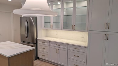 Kitchen with freestanding refrigerator, glass insert cabinets, backsplash, light stone countertops, and light wood-style floors