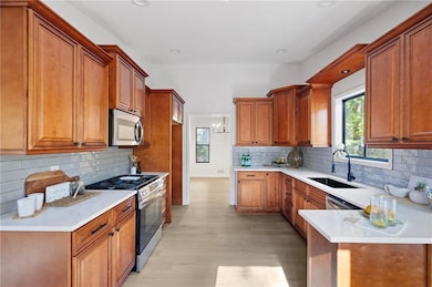 Kitchen with brown cabinetry, stainless steel appliances, backsplash, light stone counters, and recessed lighting