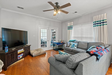 Living area with wood finished floors, ceiling fan, ornamental molding, french doors, and a textured ceiling