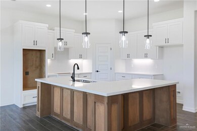 Kitchen with a kitchen island with sink, backsplash, a sink, and dark wood-style flooring