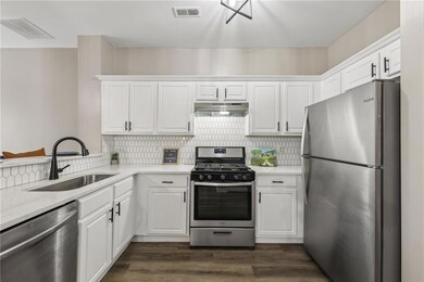 Kitchen with stainless steel appliances, under cabinet range hood, a sink, and white cabinets