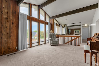 Living area featuring beamed ceiling, high vaulted ceiling, carpet floors, an upstairs landing, and wooden walls