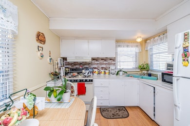 Kitchen with white appliances, light countertops, white cabinets, light wood-style flooring, and decorative backsplash