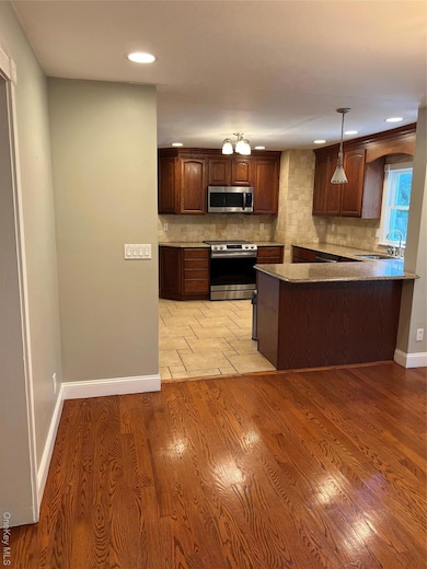 Kitchen with stainless steel range oven, tasteful backsplash, light wood-style flooring, dark stone counters, and pendant lighting