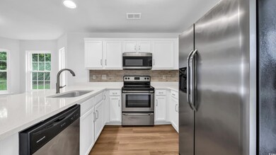 Kitchen with stainless steel appliances, light wood-type flooring, white cabinets, backsplash, and recessed lighting