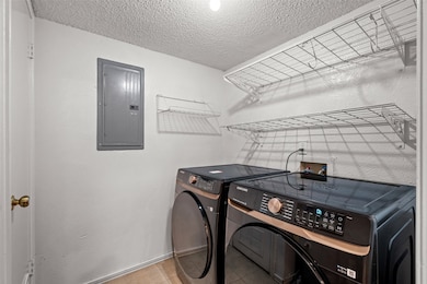 Laundry room featuring electric panel, a textured ceiling, light tile patterned floors, and washer and clothes dryer