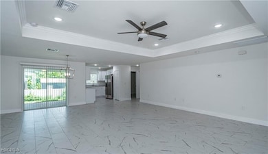 Unfurnished living room with a tray ceiling, crown molding, a ceiling fan, recessed lighting, and light marble finish flooring