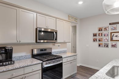 Kitchen featuring appliances with stainless steel finishes, dark wood-type flooring, and light stone counters
