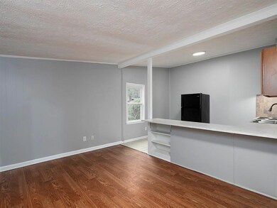 Unfurnished living room with a textured ceiling, wood finished floors, baseboards, ornamental molding, and a sink