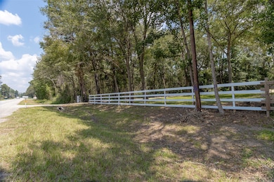 This is FM 1485 roadside property with a white wooden fence and mature trees, offering privacy and a natural setting.