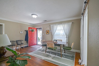Dining room with a textured ceiling, wood finished floors, visible vents, baseboards, and crown molding