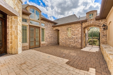 This photo showcases a charming courtyard with a rustic brick exterior and a paved patio. Large windows and French doors provide natural light, while an elegant wrought iron gate opens to a landscaped area. Ideal for outdoor entertaining and relaxation.