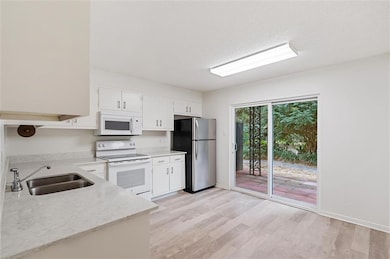 Kitchen with sink, white cabinetry, white appliances, and light wood-type flooring